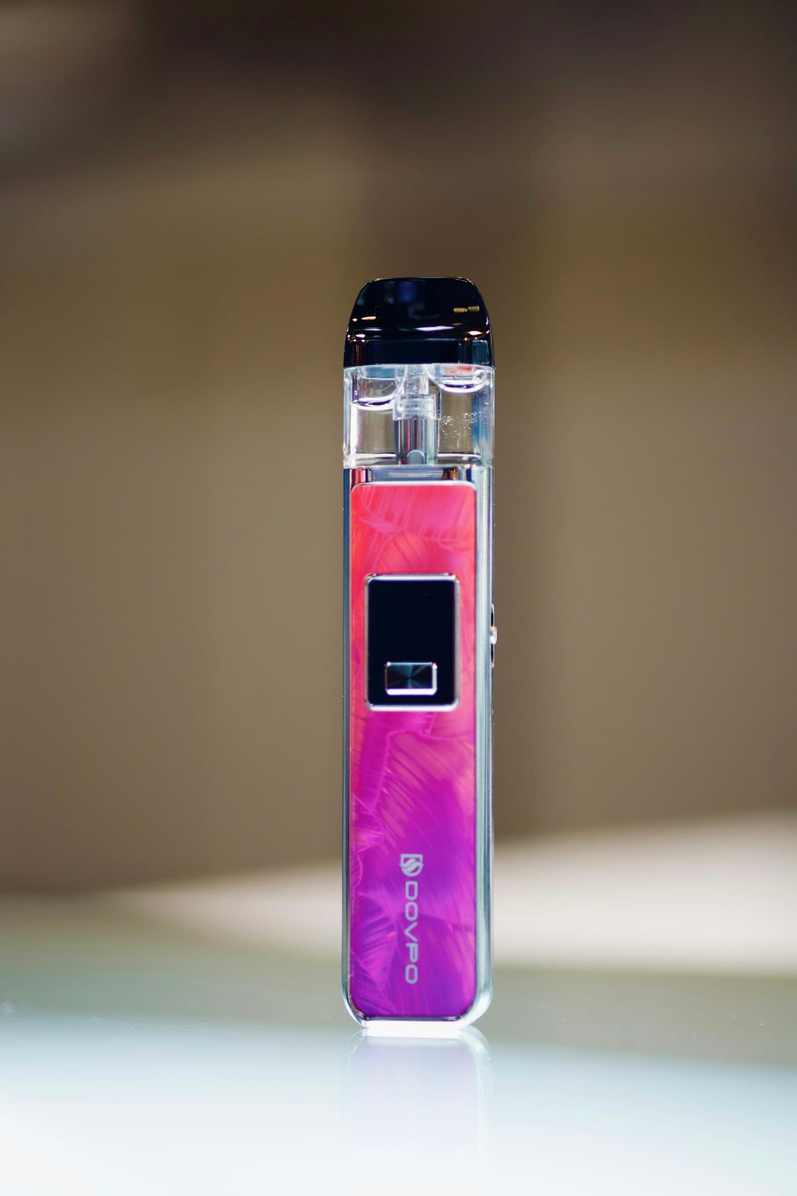 Close-up of a small purple and pink pod vape kit resting on a table